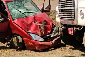 A red car’s front end has been crushed by a truck